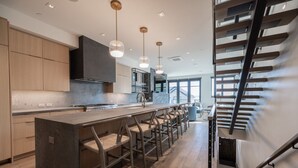Uma cozinha moderna com ilha central, banquetas e iluminação pendente.