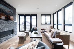 Ein modernes Wohnzimmer mit Kamin aus Stein, großen Fenstern und einer gemütlichen Sitzecke.