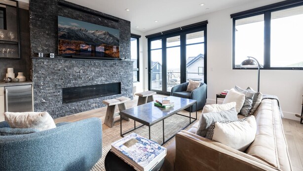 Uma sala de estar moderna com lareira de pedra, janelas amplas e móveis contemporâneos.