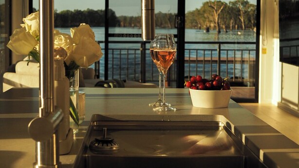A modern kitchen with a stainless steel sink, a wine glass, and a bowl of fruit.