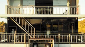 A multi-level houseboat with a balcony, a staircase, and a garage with two vehicles.