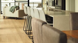 A modern kitchen with a large island, a dining area with chairs, and a view of a building through large windows.