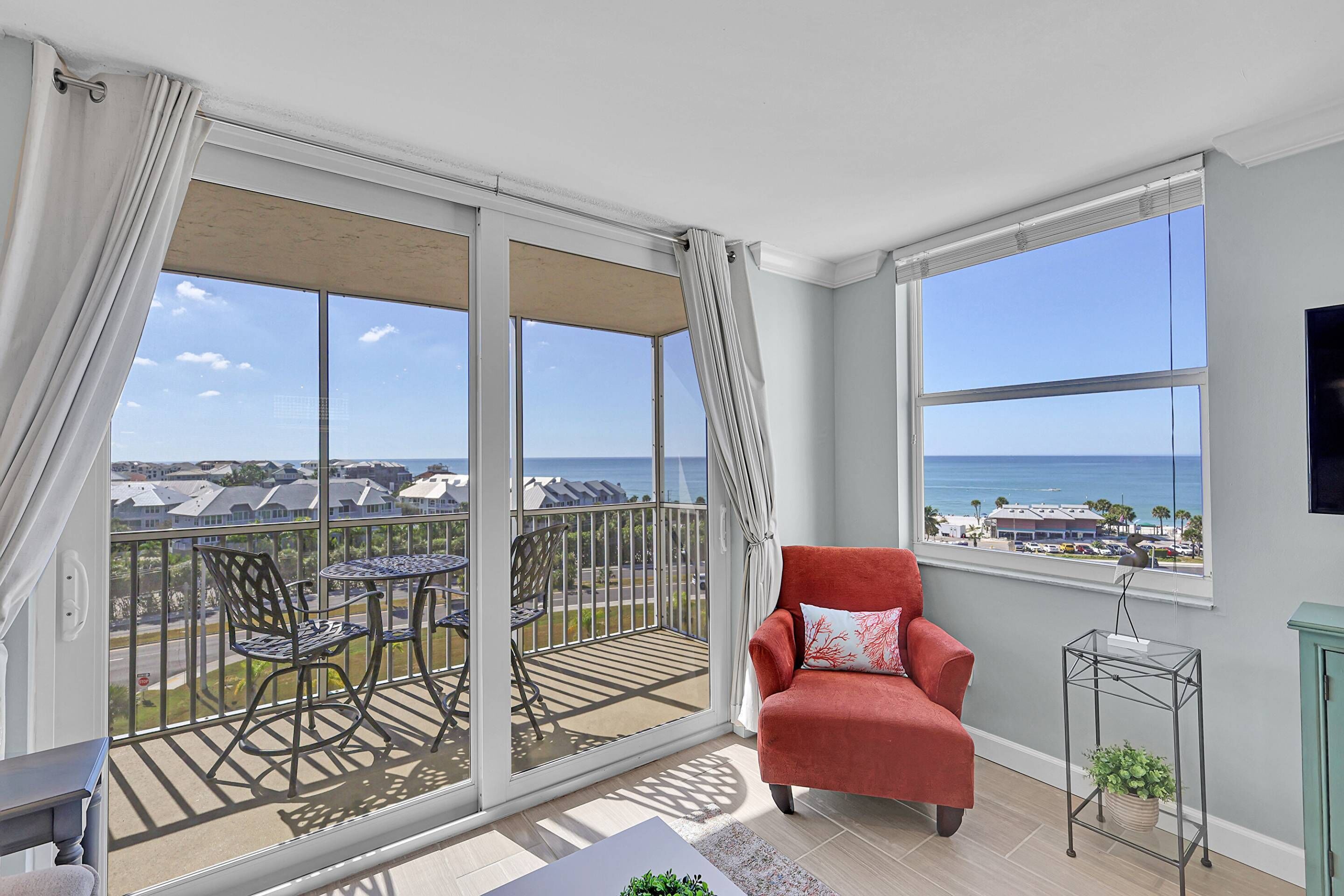 Un balcon avec vue sur l’océan, une chaise rouge et une table avec des chaises.