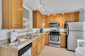 A modern kitchen with wooden cabinets, stainless steel appliances, granite countertops, and a dishwasher. - GULF & BEACH VIEWS | 8TH FLOOR BALCONY | RECLINING LOVE SEAT | KEYLESS ENTRY | STEPS TO BONITA BEACH (Bonita Springs)