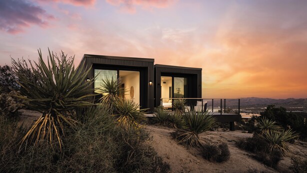 A modern house with large windows and a balcony overlooking a desert landscape.