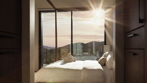 A bedroom with a large window, a bed, and wooden furniture.