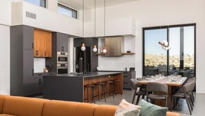 A modern kitchen with a central island, bar stools, and a dining area with a large table and chairs.
