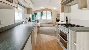Cocina compacta con pileta, estufa y alacenas, que da a una sala de estar con sofá y cortinas.