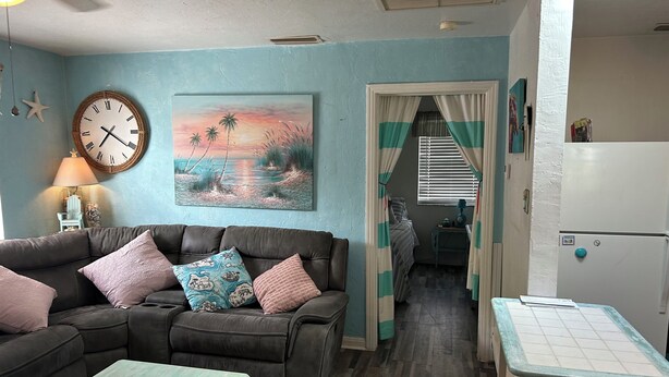 Un salon avec un canapé marron, des murs de couleur turquoise, une horloge et un tableau représentant un coucher de soleil.
