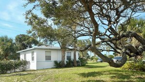 Une maison à l’extérieur blanc, entourée d’une cour verdoyante et d’un grand arbre.