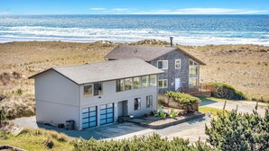 Une maison à deux étages avec un garage, située sur une falaise côtière offrant une vue sur l’océan.