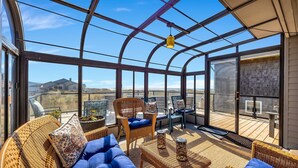 Une véranda meublée de mobilier en osier, dotée d’un toit en verre et offrant une vue sur le paysage.