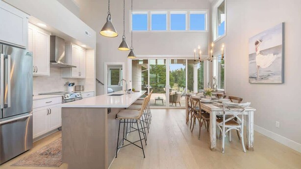 Una cocina moderna con electrodomésticos de acero inoxidable, una isla grande con taburetes de bar y un comedor con sillas blancas.