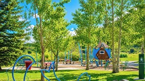 Un parque con juegos infantiles, una casita azul y un bote de basura verde.