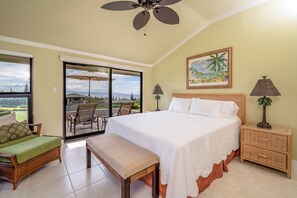 A bedroom with a bed, a bench, a nightstand, a lamp, a painting, and a view of the outdoors. - Kapalua Golf | Golf View 5 BR, Sleeps 16 | Car Incl. w/ 6+ Nights | KGV ML-2321 by KBM (Lahaina)