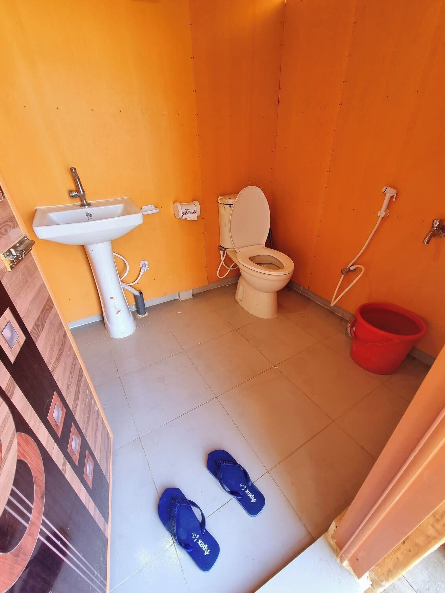 A small bathroom with a sink, toilet, and red bucket.