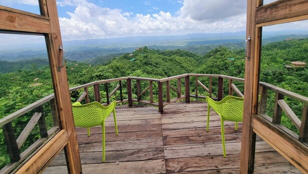 A wooden deck with two green chairs facing a scenic view of a lush valley and distant mountains.