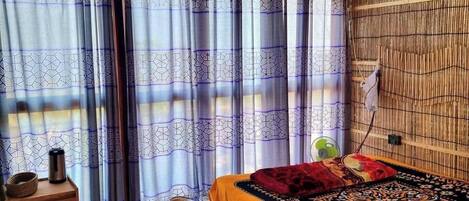 A room with a bed, a small table, and a window with patterned curtains.