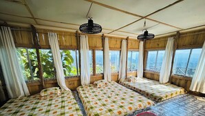 A room with three beds, large windows, and a view of greenery.