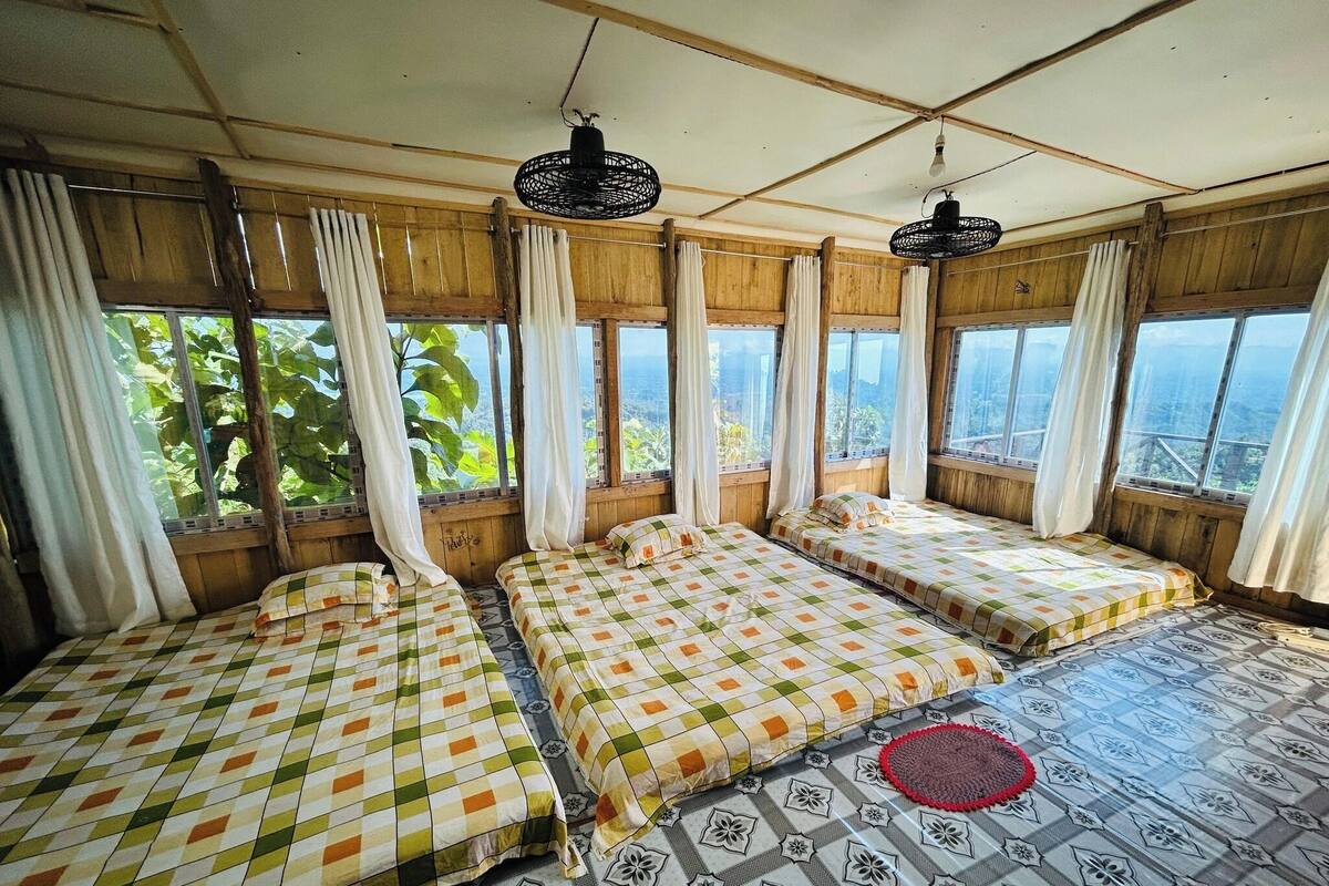Habitación con tres camas, ventanas amplias y vista a zonas verdes.