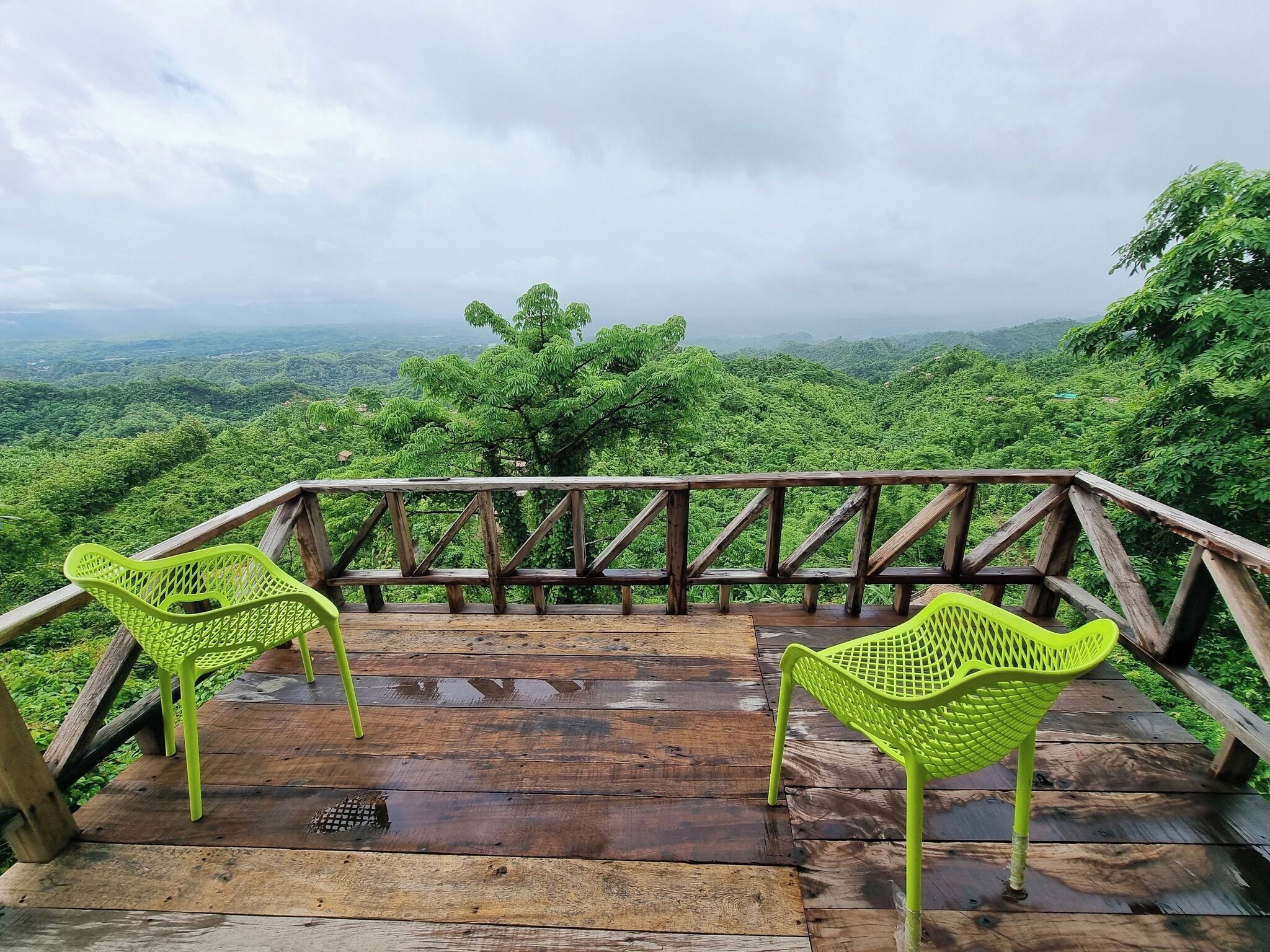 A wooden deck with two bright green chairs overlooking a lush green landscape.