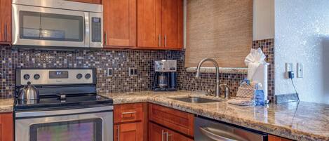 A kitchen with wooden cabinets, a stainless steel microwave, a stove, a coffee maker, and a sink.