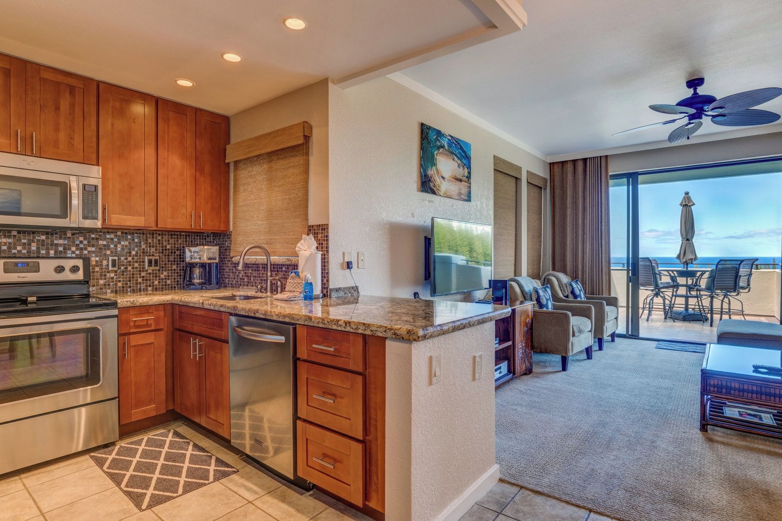 A modern kitchen with a microwave, stove, and dishwasher, a dining area with a TV, and a balcony with a view.
