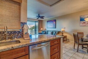 A kitchen with a built-in dishwasher, a dining area with a table and chairs, and a ceiling fan. - Kapalua Golf | Golf View 5 BR, Sleeps 15 | Car Incl. w/ 6+ Nights | KGV ML-2333 by KBM (Lahaina)