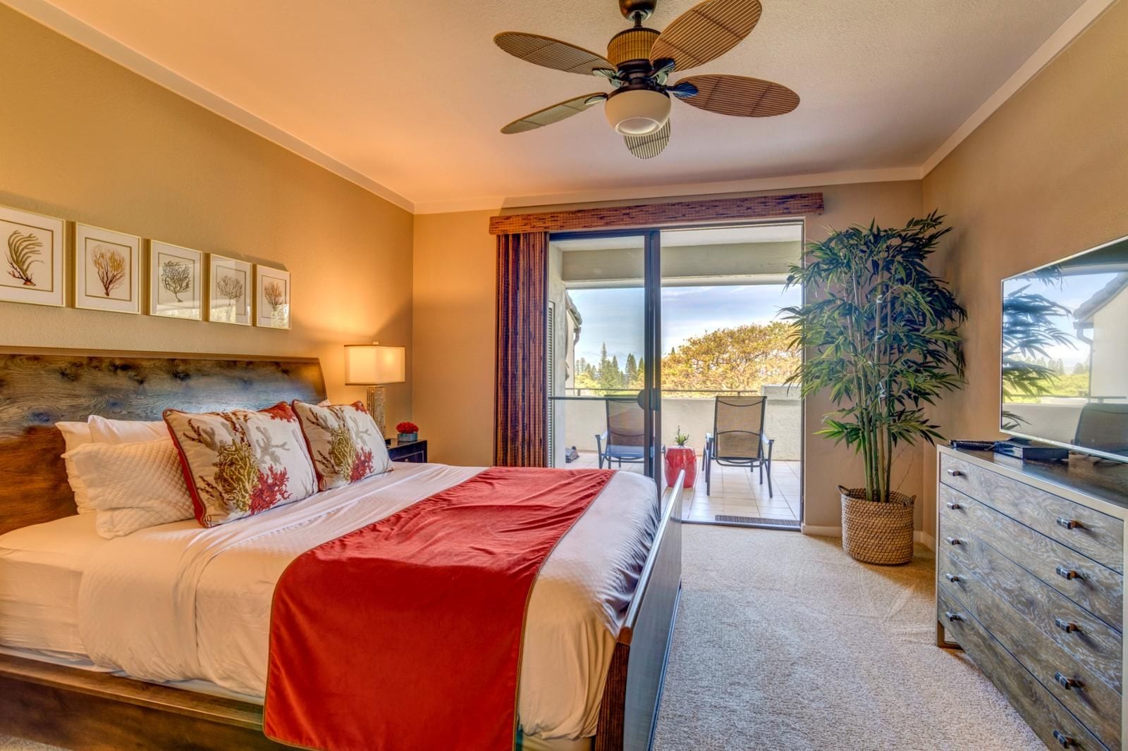 A hotel room with a bed, a ceiling fan, a TV, a dresser, and a balcony with a view.