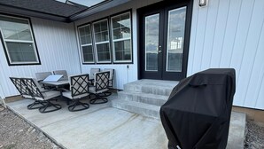 Una veranda con barbecue, posti a sedere all'aperto e una porta con gradini che conducono a un'area coperta.