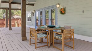 A covered outdoor dining area with a table and chairs, wooden beams, and a view of a house through glass doors. - Spacious Modernized Historic Home 3 Minute Walk from Square (Georgetown)