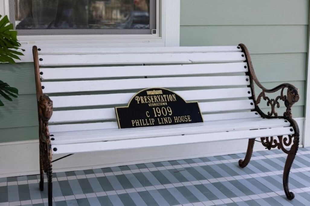 A white bench with a black plaque reading "Preservation Georgetown c 1909 Phillip Lind House."