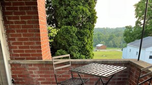 Un espace patio agrémenté d’un mur en briques, de deux chaises en métal, d’une table en métal et d’une chaise bleue.