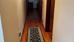 Un couloir doté d’un plancher en bois, d’un tapis à motifs et d’une porte donnant sur une autre pièce.