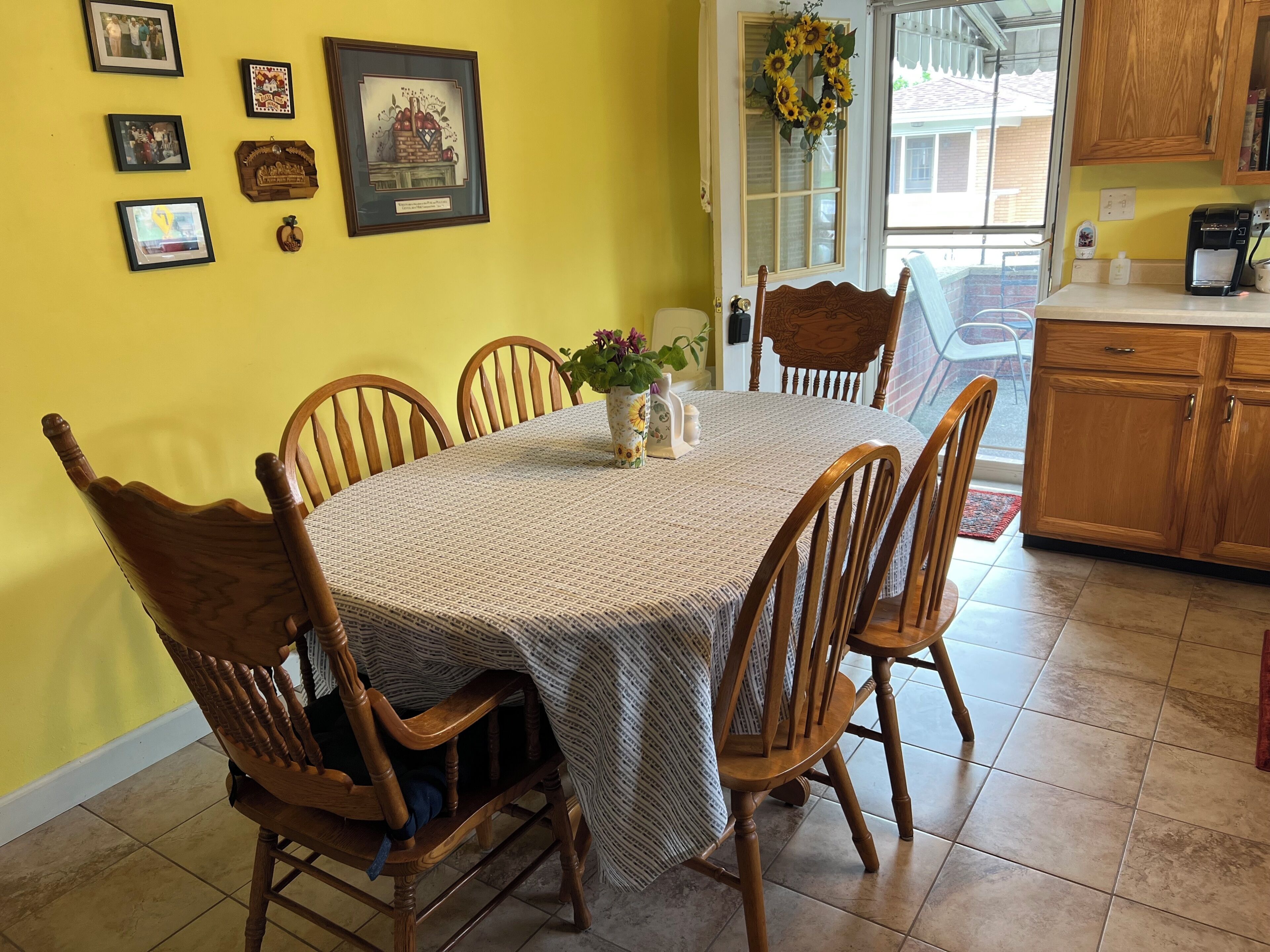 Un coin repas avec une table ronde, six chaises en bois, un vase de fleurs et des tableaux encadrés accrochés au mur.