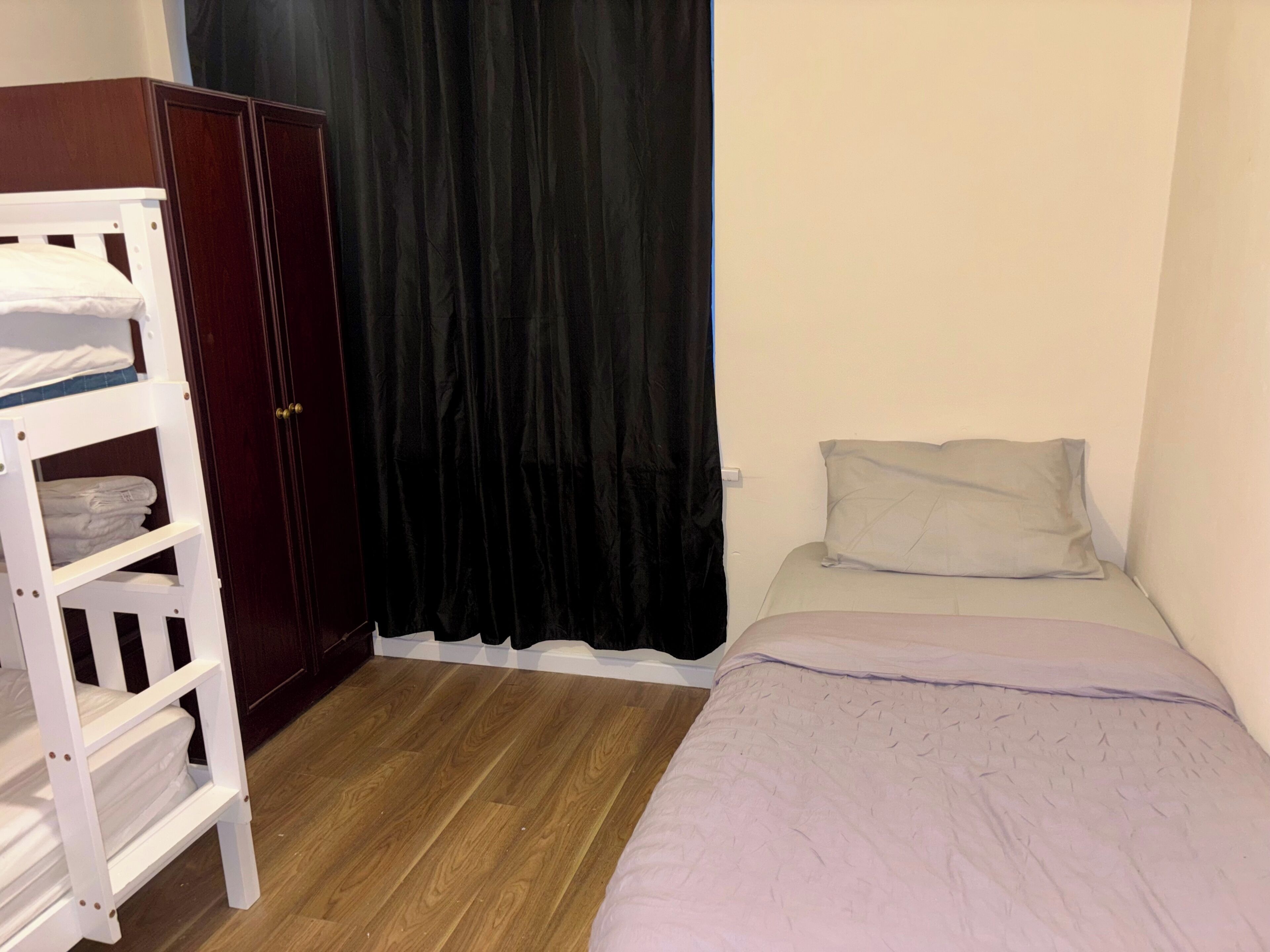 Une chambre avec un lit superposé, une armoire, un lit simple avec un oreiller et un rideau noir.
