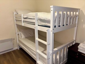 A bunk bed with white bedding, a heater, and a wooden nightstand with a folded towel. - Larches Lane Retreat - Sleeps 5 - Wolverhampton (Wolverhampton)