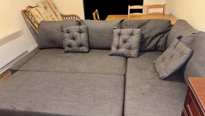 A grey sectional sofa with tufted pillows, a wooden dining table, and a chair.