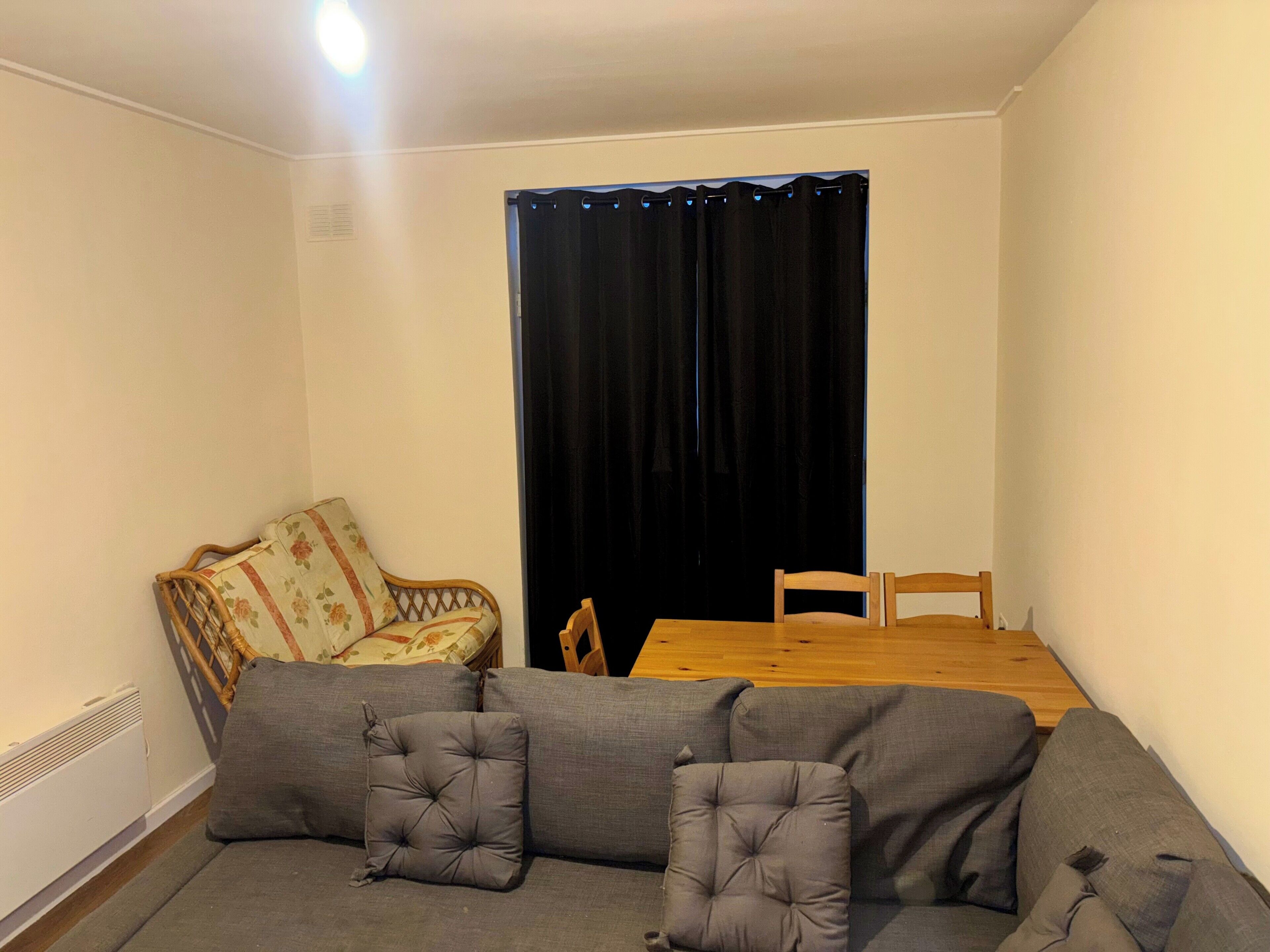 Una sala de estar con sofá, una silla, una mesa y una cortina negra.