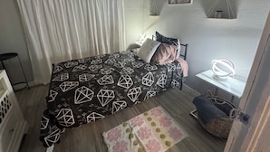 Et soveværelse med en seng, et natbord, en lampe, et tæppe og en billedvæg.