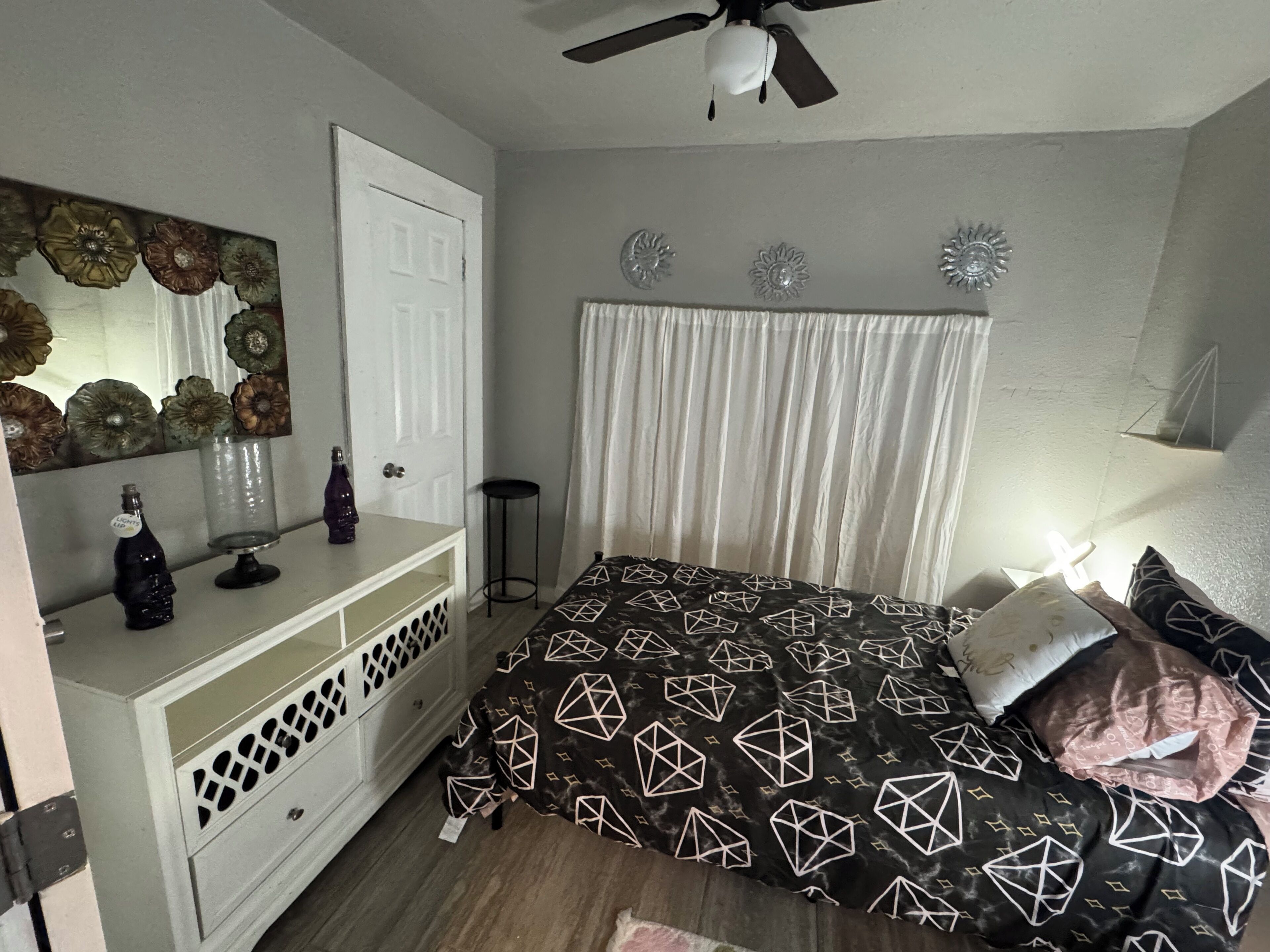 Une chambre à coucher avec un lit, une commode, un miroir et un ventilateur de plafond.