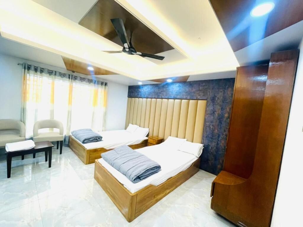 Habitación de hotel con dos camas, ventilador de techo, cabecero de madera, escritorio y una silla.