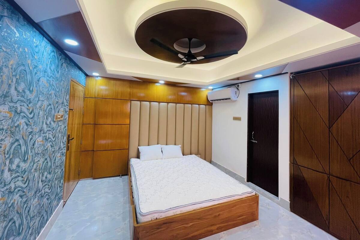 A bedroom with a bed, a ceiling fan, wooden wardrobe, and a wardrobe with geometric patterns.