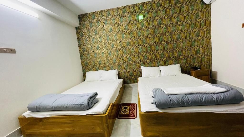 Ein Zimmer mit zwei Holzbetten, jedes mit weißer Bettwäsche und Kissen. Die Wände sind mit einem geometrischen Muster tapeziert.