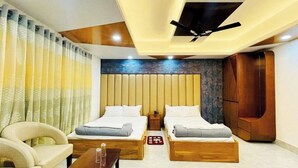 A modern hotel room with two beds, a sofa, a wooden coffee table, and a ceiling fan. - Hotel Sonar Bangla Rangamati (Rangamati Sadar)