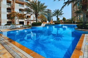 Ein Swimmingpool, umgeben von Palmen und einem mehrstöckigen Gebäude mit Balkonen.