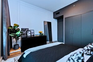 A modern bedroom with a large bed, a dresser, a mirror, and a wardrobe. - Luxe 1-BR w/ Sunset, Golf & Lake View in The Greens (The Greens)