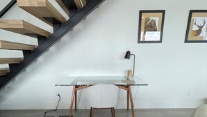 Un espace de bureau moderne avec un bureau en verre, une chaise, un escalier et deux tableaux encadrés accrochés au mur.