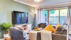 A living room with a flat-screen TV, leather chairs, a sofa with cushions, a coffee table with a tray, a floor lamp, and a potted plant. - Bring Your Pet! Snowbird Haven w/ Community Pool! (Scottsdale)