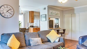 A living room with a grey sofa, yellow and grey cushions, a coffee table with pumpkins and candles, a clock on the wall, and a kitchen in the background. - Bring Your Pet! Snowbird Haven w/ Community Pool! (Scottsdale)
